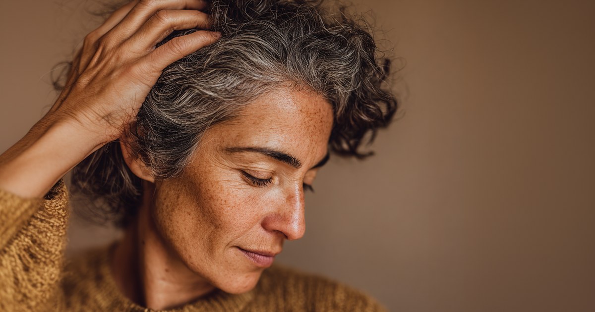 Femme aux cheveux grisonnants passant la main dans sa chevelure — rôle de la L-cystéine dans la solidité du cheveu