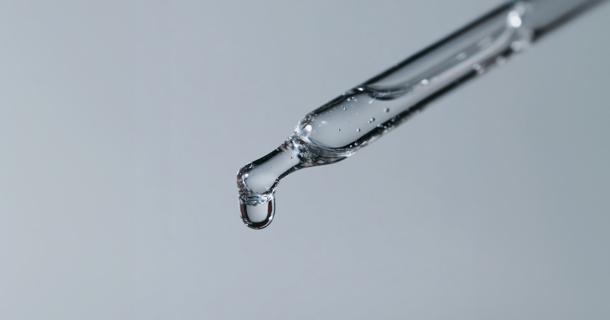 Pipette en verre laissant tomber une goutte de sérum transparent, illustrant une lotion topique au Procapil